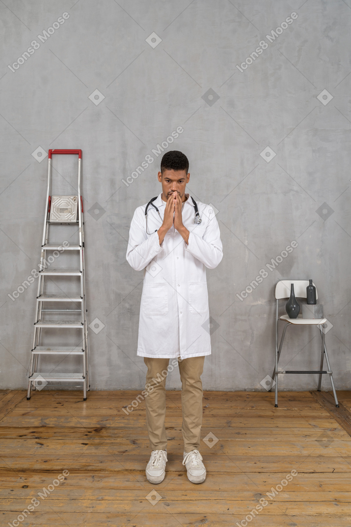 사다리와 의자가있는 방에 서있는 걱정 된 젊은 의사의 전면보기