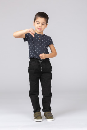 Вид спереди симпатичного мальчика в повседневной одежде, показывающего большой палец вниз