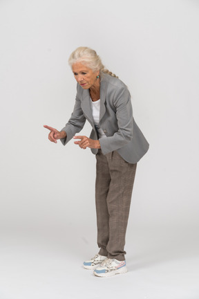 Vista lateral de uma senhora idosa de terno se curvando e mostrando um sinal de alerta