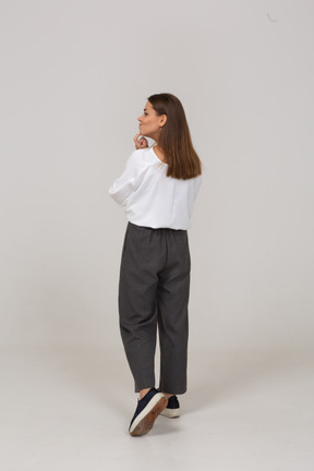 Vista posterior de tres cuartos de una joven pensativa en ropa de oficina tocando la barbilla