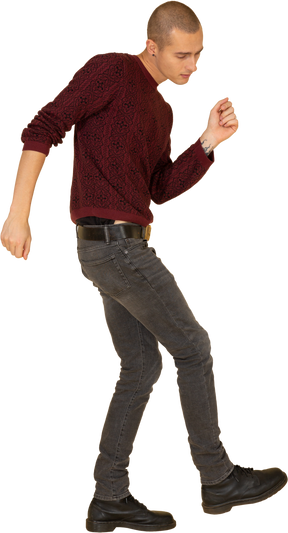 Вид сбоку танцующего молодого человека в красном пуловере, поднимающего ногу