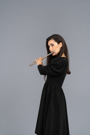 フルートを演奏する黒いドレスを着た真面目な若い女性の4分の3のビュー