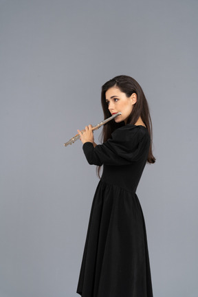 Three-quarter view of a serious young lady in black dress playing the flute