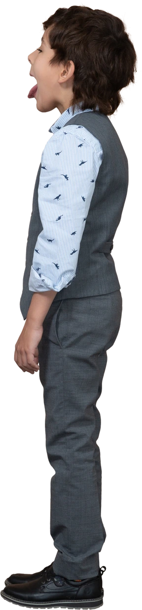 Side view of a cute boy in grey suit showing tongue
