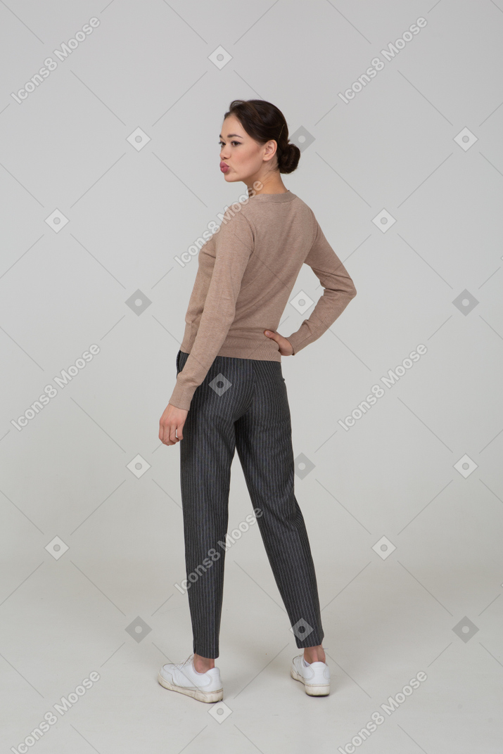 Vue arrière des trois quarts d'une jeune femme debout encore en pull et pantalon mettant la main sur la hanche et bouder