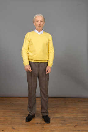 Vista frontal de um velho surpreso de blusa amarela fazendo uma careta e olhando para a câmera