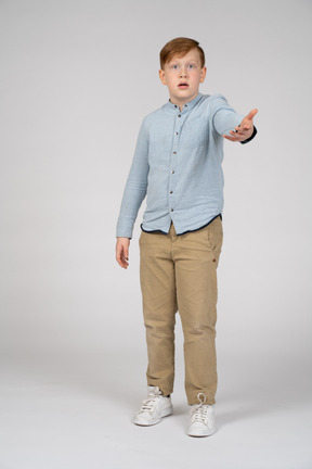 Vista frontal de um menino impressionado, apontando para a câmera com a mão