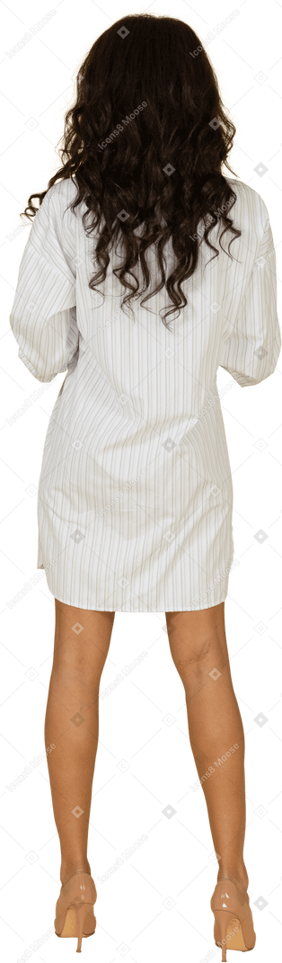 Vista traseira de uma jovem mulher de pele escura abotoando seu vestido branco