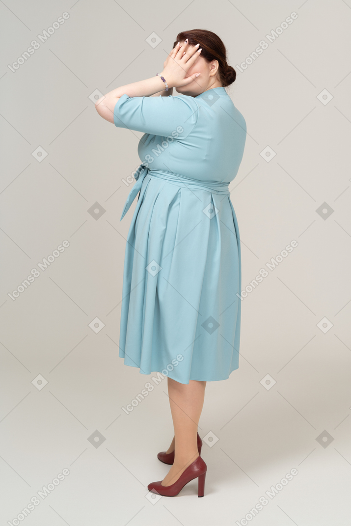 Side view of a woman in blue dress closing eyes with hands