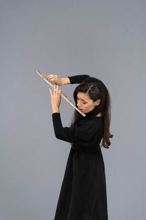 Three-quarter view of a serious young lady in black dress playing the flute