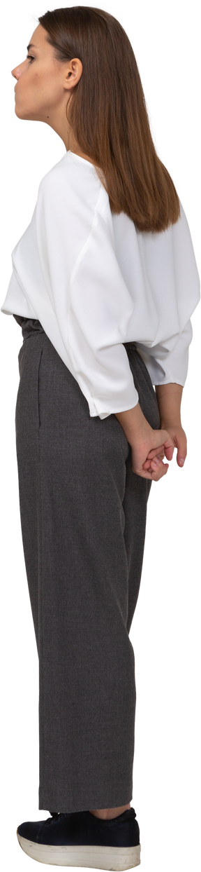 Three-quarter back view of a young lady in office clothing holding hands behind