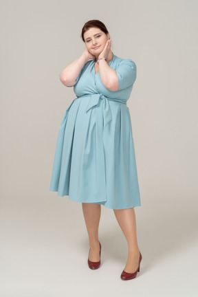 Vista frontal de uma mulher de vestido azul posando com as mãos no pescoço