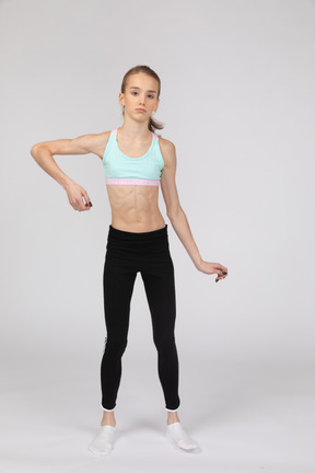 Vista frontal de uma adolescente em roupas esportivas, olhando para a câmera enquanto dobra o braço