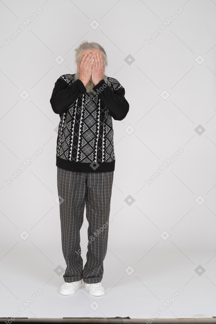 Elderly man facing the camera and covering his face with his hands