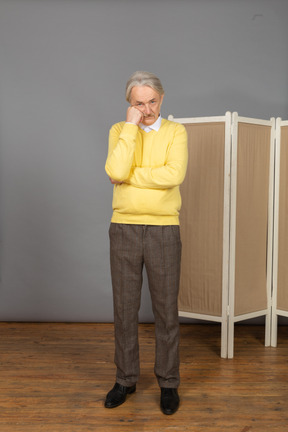 Front view of a thoughtful old man near the screen touching chin