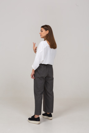 Vista posterior de tres cuartos de una joven en ropa de oficina mostrando dos dedos