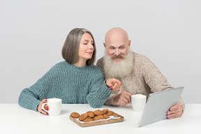 Pareja de ancianos tomando un café y mirando la película en la tableta