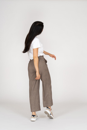 Vista posteriore di tre quarti di una giovane donna in calzoni e maglietta che si allontana