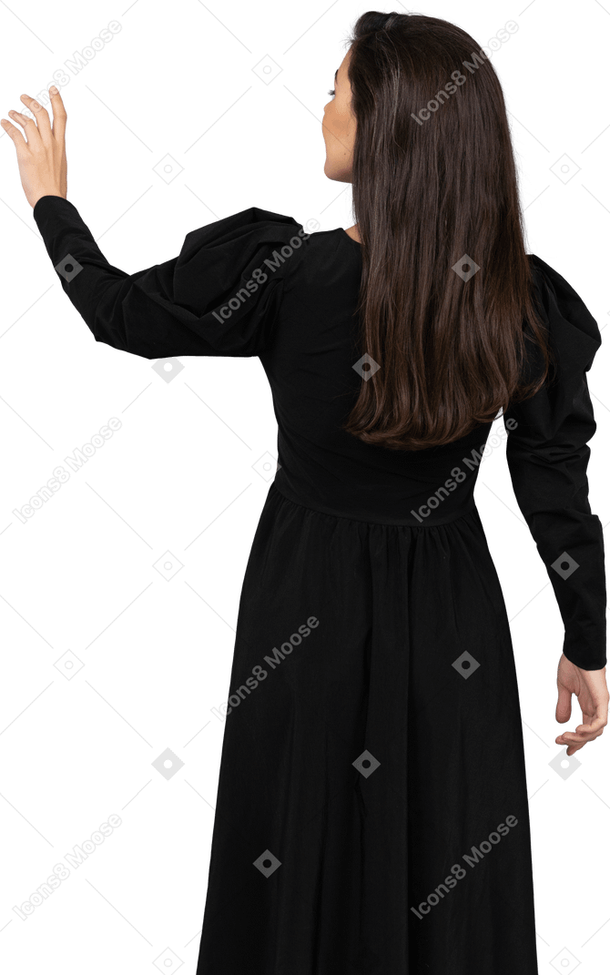 Вид сзади молодой леди в черном платье, поднимающей руку