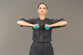 Front view of young woman in a jumpsuit doing exercises with dumbbells