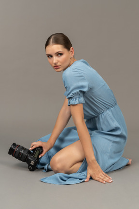 Vista laterale di una giovane donna in abito blu seduta su un pavimento con telecamera