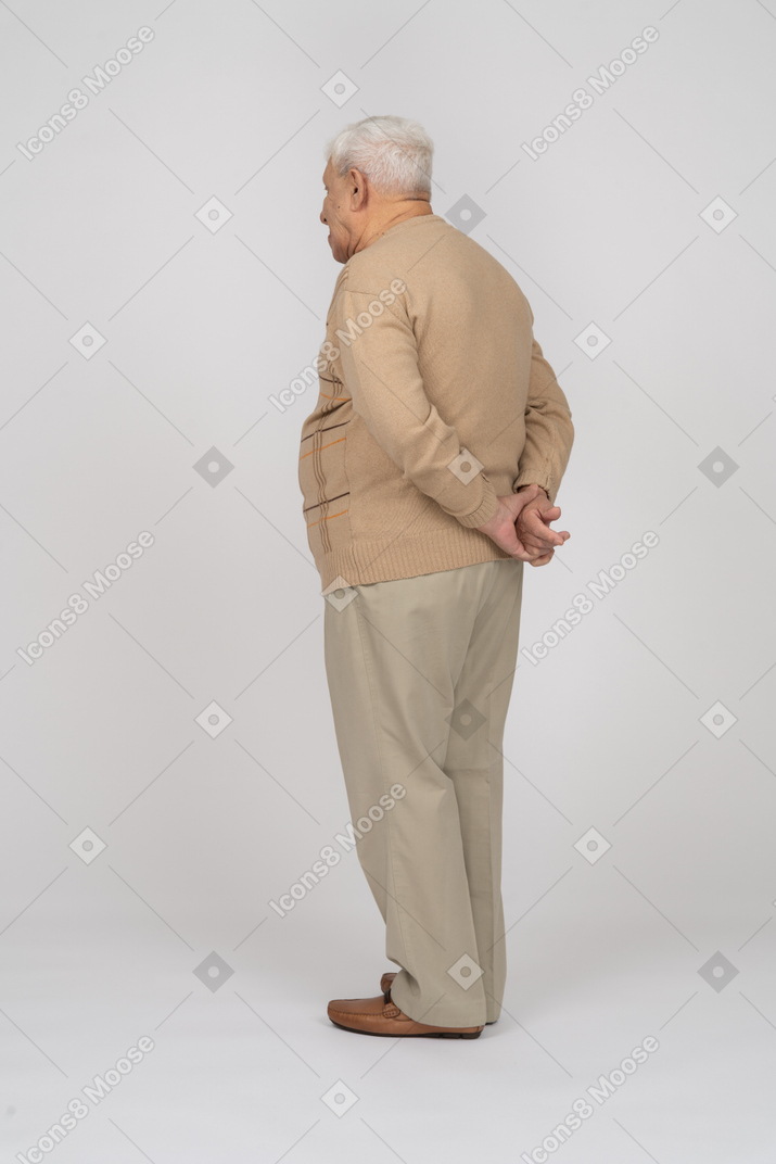 Vista lateral de un anciano con ropa informal posando con las manos detrás de la espalda