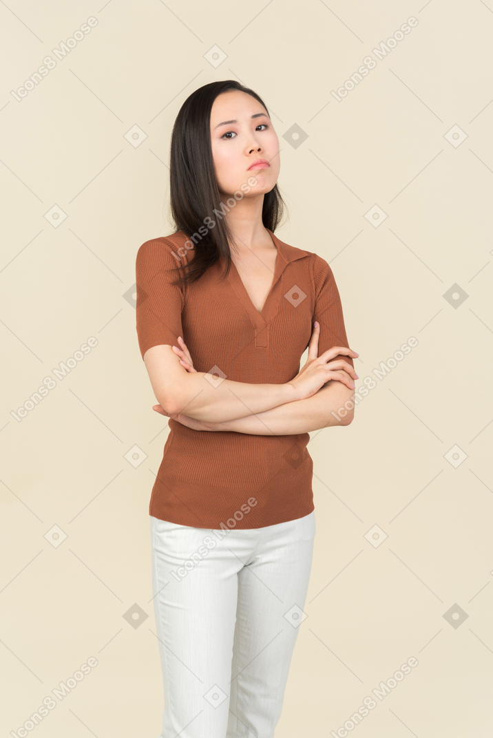 Sérieuse jeune femme asiatique debout avec les mains croisées