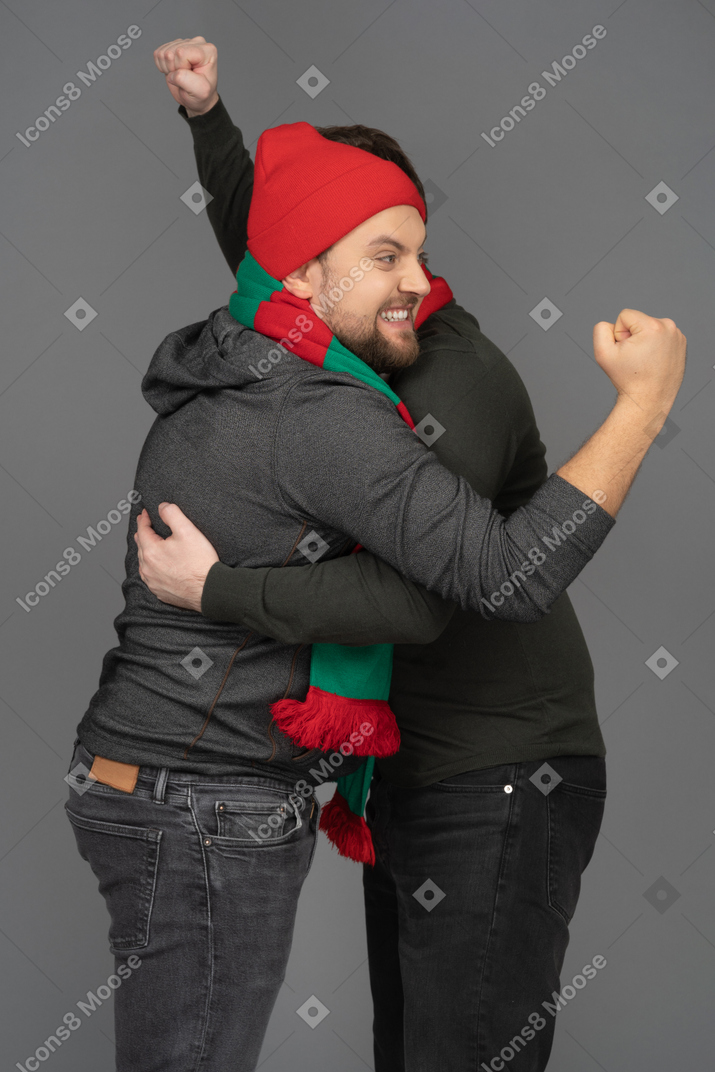 Side view of two emotional hugging male football fans clenching fists