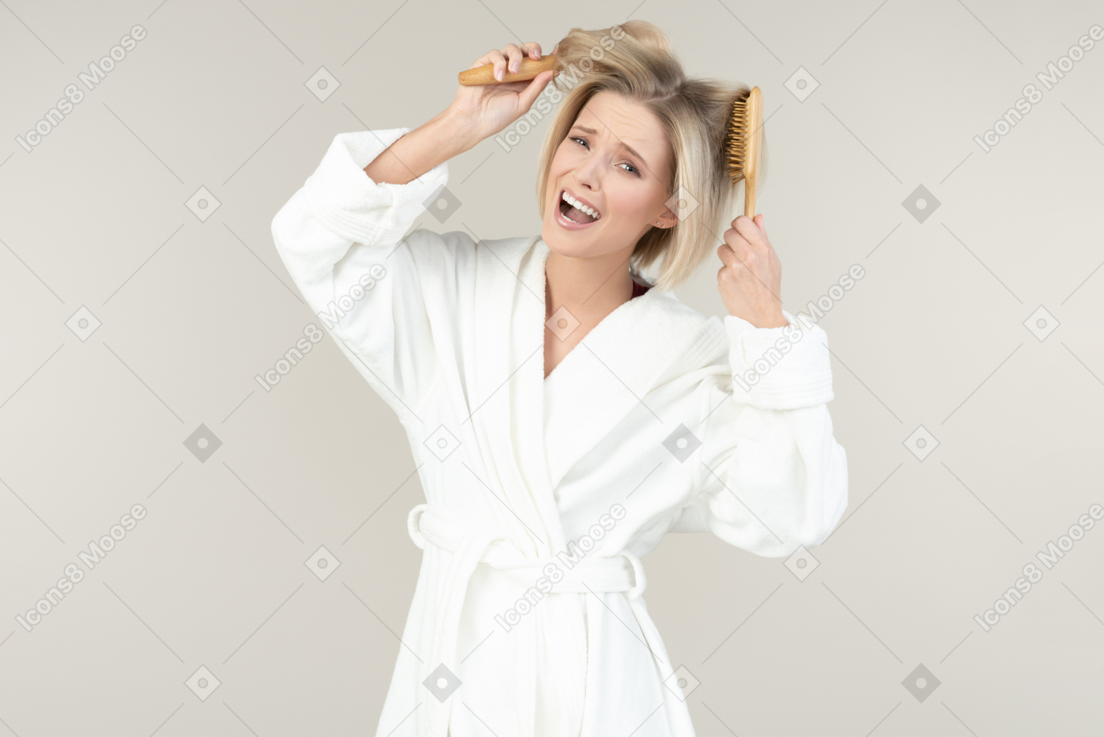 Junge blonde frau in einem weißen bademantel, der mit allen arten toilettenartikeln aufwirft