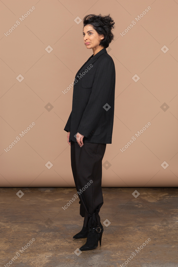 Vista di tre quarti di una donna d'affari dispiaciuta smorfie in un vestito nero che osserva da parte