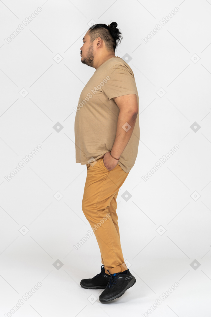 Homem asiático pensativo em pé no perfil com as mãos nos bolsos