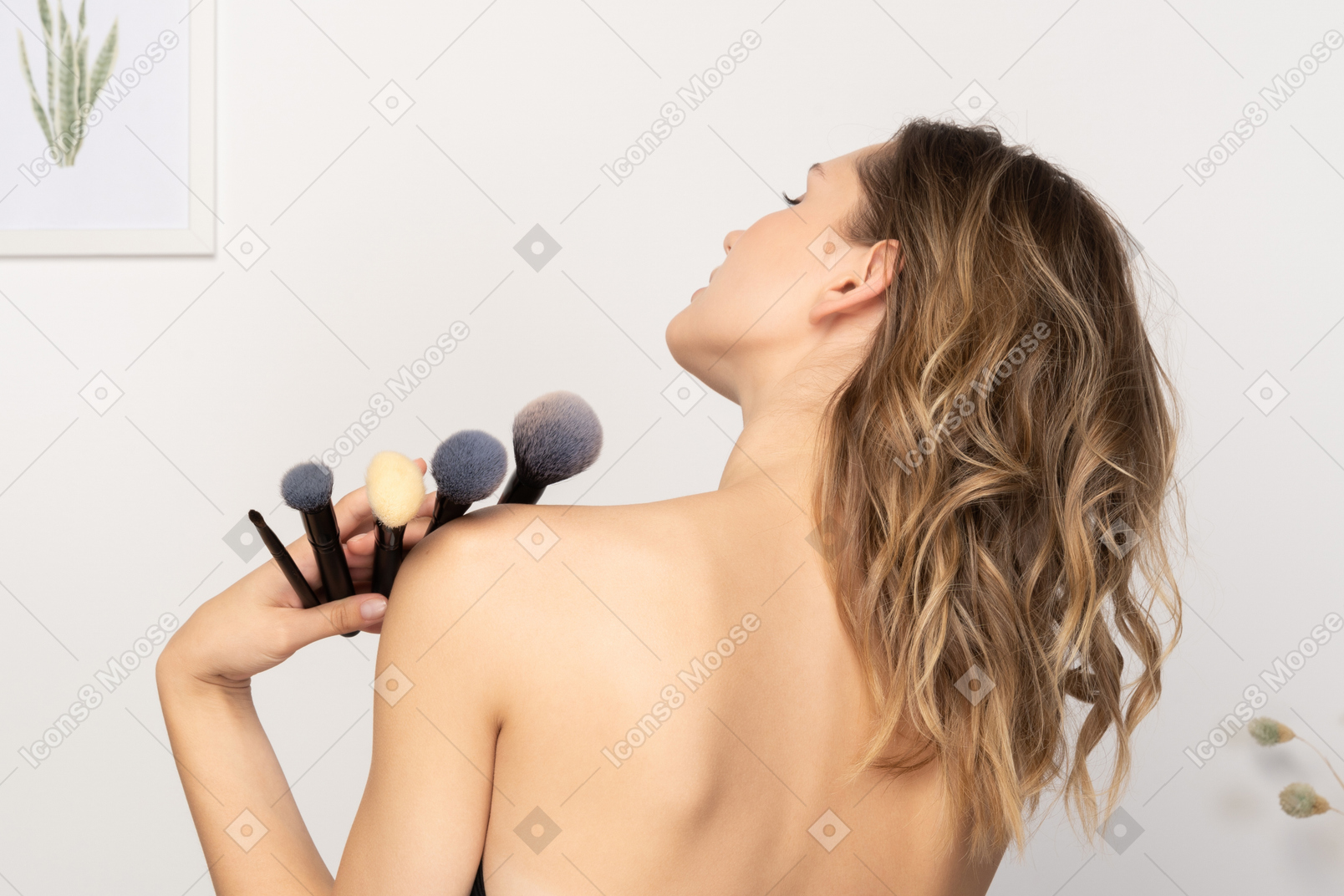 Vista traseira de uma jovem sensual segurando pincéis de maquiagem
