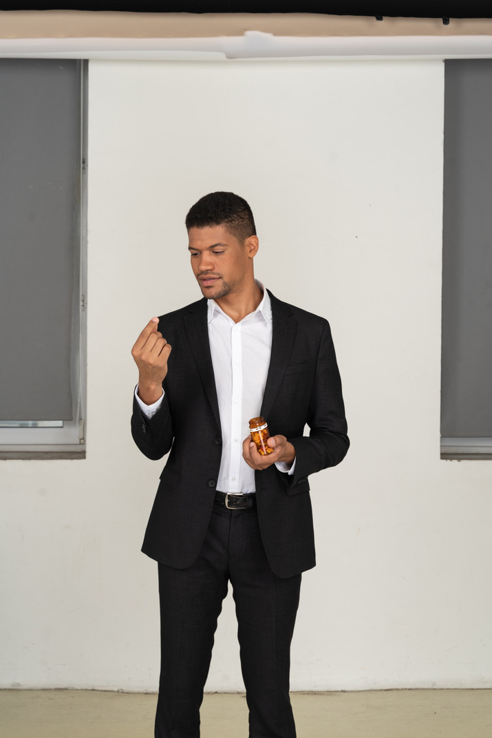 Young man in black suit looking at pills bottle he's holding