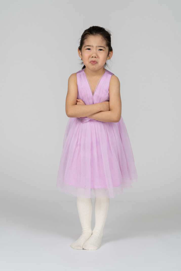 Little girl in pink dress standing disappointed with her arms crossed