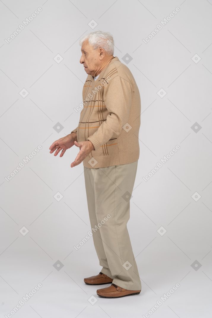 伸ばした腕で立っているカジュアルな服装の老人の側面図