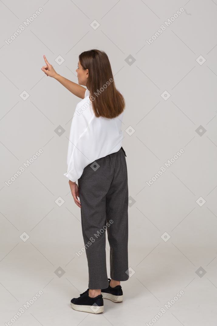 Back view of a young lady in office clothing pointing finger up