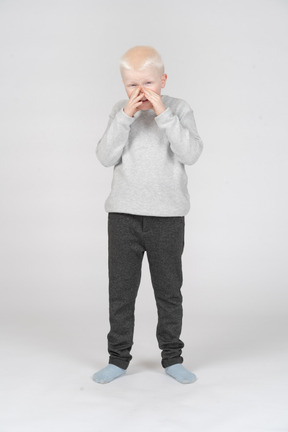 Vista frontal de un niño cubriendo su boca con las manos y riendo