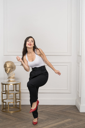 A figura intera di una giovane donna sorridente che balla vicino alla scultura greca dorata