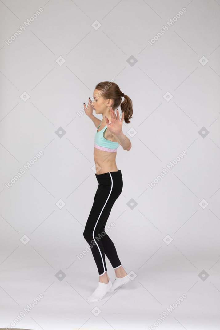 Side view of a teen girl in sportswear balancing on tiptoes while raising hands
