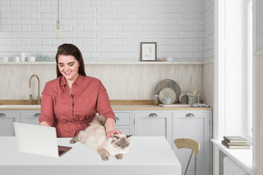 A woman sitting at a kitchen counter petting a cat