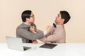 Two young nerds sitting at the table and punching each other into the face