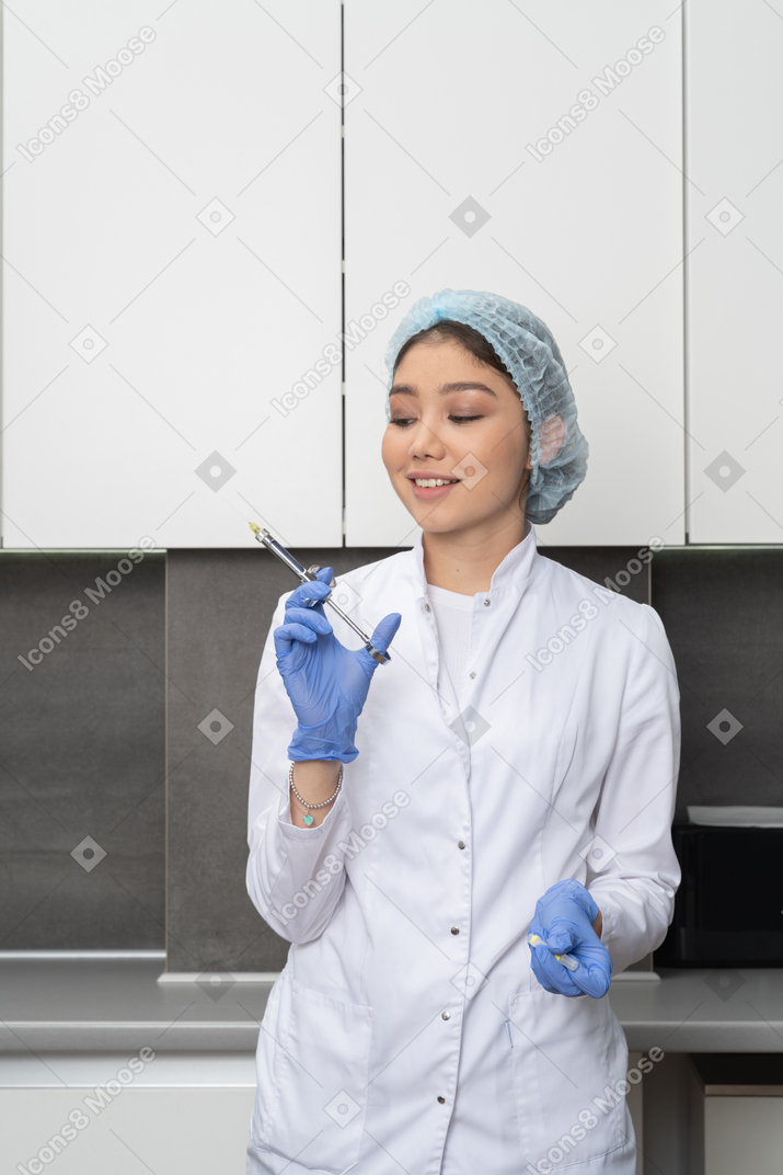 Front view of a smiling nurse holding a syringe and looking aside