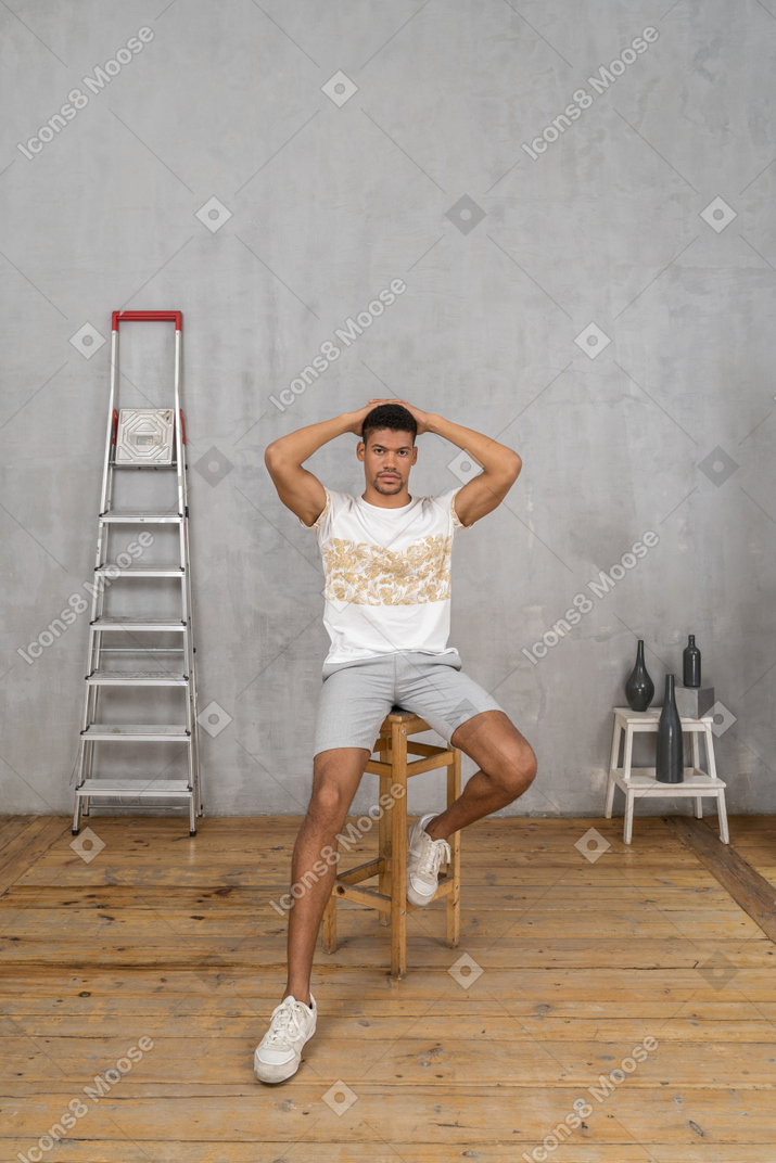Молодой человек сидит на стуле и держит руку на затылке