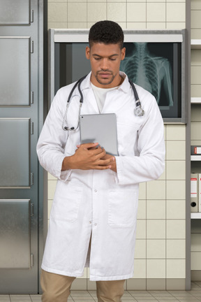 Nachdenklicher arzt, der mit seiner tablette vor einer röntgenaufnahme steht