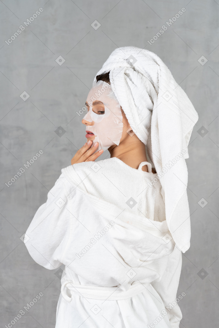 Vista trasera de una mujer en bata de baño con una máscara facial puesta