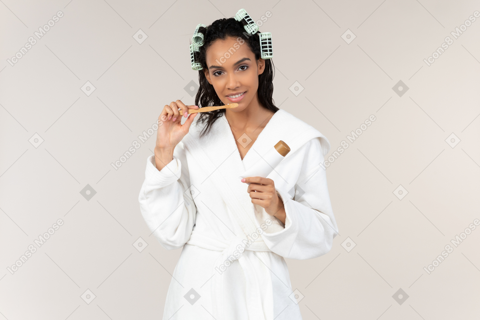 Young woman in bathrobe and with hair curlers brushing teeth