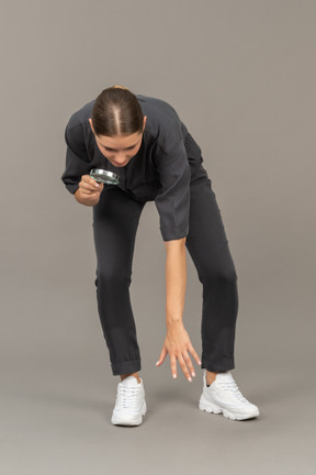 Front view of a young woman in a jumpsuit holding a magnifying glass