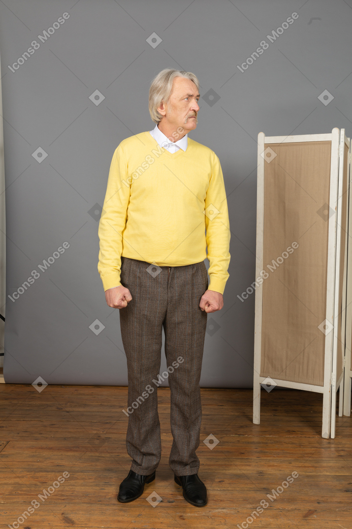 Front view of a displeased old man clenching fists while looking aside