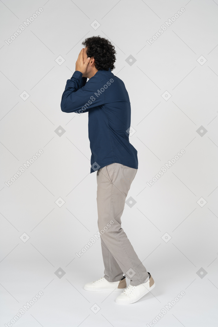 Vista lateral de um homem com roupas casuais cobrindo o rosto com as mãos