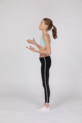 Vista lateral de uma adolescente em roupas esportivas levantando as mãos e olhando para o lado